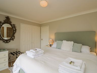 A bedroom with a bed with folded towels a bedside table with a lamp and a round decorative mirror on the wall at The River House Avon Valley Stonehenge with fishing Salisbury