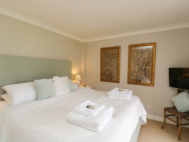 A bedroom with a bed with pillows and folded towels two framed pictures on the wall and a chair with a cushion at The River House Avon Valley Stonehenge with fishing Salisbury