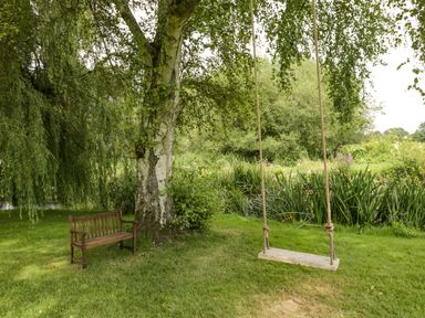 A wooden bench and a swing hanging from a tree near a pond at The River House Avon Valley Stonehenge with fishing Salisbury