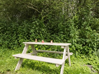 A white picnic table with three small bear figurines on top surrounded by green foliage at The River House Avon Valley Stonehenge with fishing in Salisbury