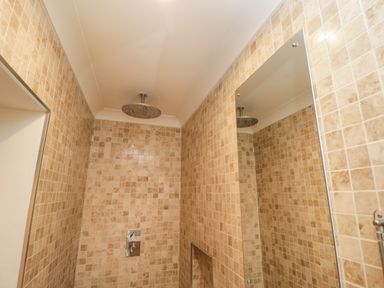 A shower area with beige tiled walls a round ceiling-mounted showerhead and a wall-mounted control panel at The River House Avon Valley Stonehenge with fishing Salisbury