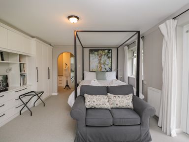 A bedroom with a four poster bed and a grey sofa in front of it at The River House Avon Valley Stonehenge with fishing Salisbury