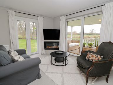 A living room with sofas a round coffee table a fireplace and large windows at The River House Avon Valley Stonehenge with fishing in Salisbury