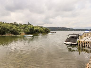 A lake with boats anchored near a dock and trees in the background at Black Dog Lodge in Thirlmere 3 White Cross Bay near Windermere