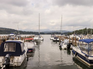 A marina with boats docked on both sides of a wooden pier with hills and trees in the background at Black Dog Lodge Thirlmere 3 White Cross Bay near Windermere
