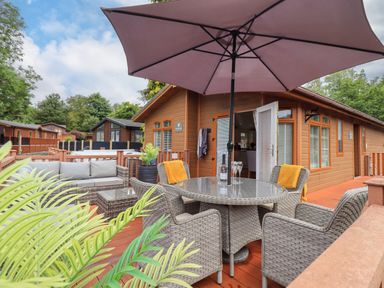 A patio with wicker furniture including a round table with an umbrella and chairs at Black Dog Lodge in Thirlmere 3 White Cross Bay near Windermere