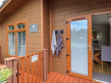 Exterior wooden deck with towels hanging near a glass door leading to a dining area at Black Dog Lodge Thirlmere 3 White Cross Bay near Windermere