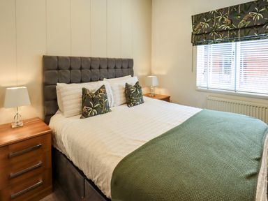 A bedroom with a bed with decorative pillows bedside tables with lamps and a window with blinds and a patterned roman shade at Black Dog Lodge Thirlmere 3 White Cross Bay near Windermere