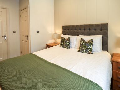 A bedroom with a bed with green and white bedding two bedside tables with lamps and two doors at Black Dog Lodge Thirlmere 3 White Cross Bay near Windermere