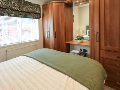 A bedroom with wooden wardrobes a bed with a green blanket and a window with blinds at Black Dog Lodge Thirlmere 3 White Cross Bay near Windermere