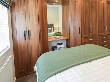A bedroom with wooden wardrobes a bed with green blanket and a window with blinds at Black Dog Lodge Thirlmere 3 White Cross Bay near Windermere