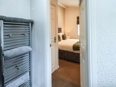 A view into a bedroom with a bed and pillows from a bathroom with a heated towel rail at Black Dog Lodge Thirlmere 3 White Cross Bay near Windermere
