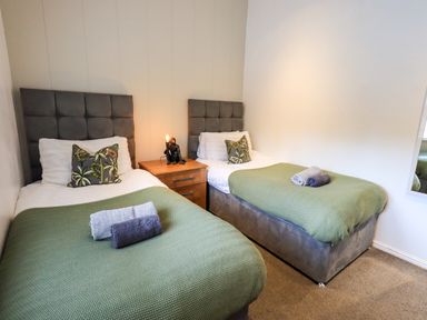 A bedroom with two single beds green blankets and a bedside table with a lamp at Black Dog Lodge Thirlmere 3 White Cross Bay near Windermere