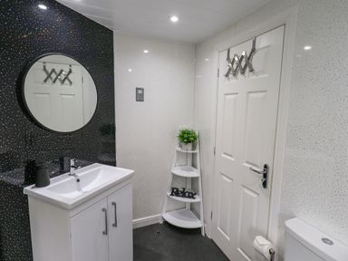 A bathroom with a round mirror above a sink cabinet a white door with hooks and a corner shelf with a plant and relax sign at Black Dog Lodge Thirlmere 3 White Cross Bay near Windermere