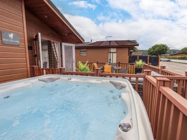 An outdoor hot tub on a wooden deck with patio furniture and umbrella at Black Dog Lodge in Thirlmere 3 White Cross Bay near Windermere