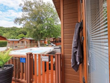 An outdoor hot tub on a wooden deck with a safety gate and towel hanging on wooden cabin door at Black Dog Lodge Thirlmere 3 White Cross Bay near Windermere