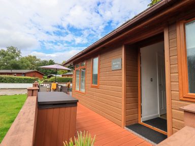 Exterior view of a wooden lodge with a small porch and outdoor seating area with umbrella at Black Dog Lodge in Thirlmere 3 White Cross Bay near Windermere