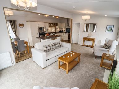 A living room with a sofa and armchair a wooden coffee table and side tables an open kitchen and dining area with chairs at Bramblewick in Runswick Bay near Staithes