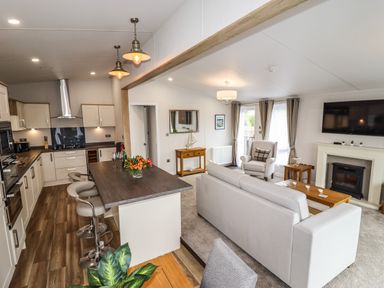 An open plan kitchen and living room with bar stools kitchen cabinets sofa armchair and a fireplace at Bramblewick in Runswick Bay near Staithes