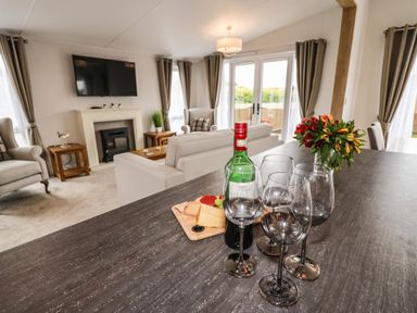 A living room with a sofa chairs fireplace a mounted television and a table with wine glasses a bottle of wine flowers and cheese at Bramblewick in Runswick Bay near Staithes