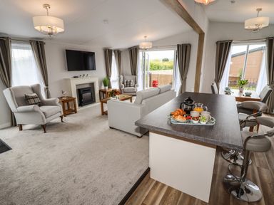 An open plan living area with armchairs sofas a television and a kitchen island with breakfast on a tray at Bramblewick in Runswick Bay near Staithes