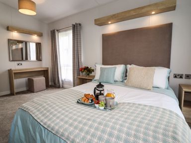 A bedroom with a bed set with pillows and blanket a tray with breakfast a dressing table flowers and curtains at Bramblewick in Runswick Bay near Staithes