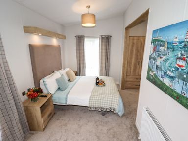 A bedroom with a bed bedside tables curtains a wardrobe and a painting at Bramblewick in Runswick Bay near Staithes