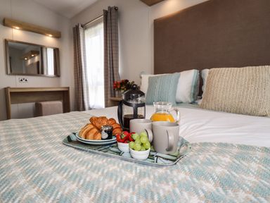 A breakfast tray with croissants coffee orange juice and fruit on a bed in a bedroom with a dresser and mirror at Bramblewick in Runswick Bay near Staithes