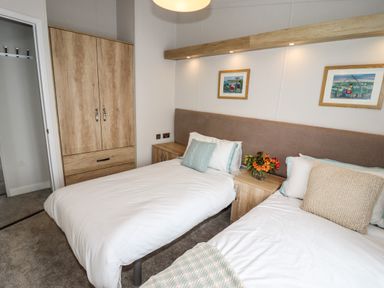 A bedroom with two single beds a wooden wardrobe and nightstands with flowers at Bramblewick in Runswick Bay near Staithes