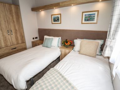 A bedroom with two single beds a wooden wardrobe and bedside tables with flowers at Bramblewick in Runswick Bay near Staithes