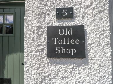 A textured white wall with a black house number 5 plate and Old Toffee Shop sign beside a green door at Old Toffee Shop in Ambleside