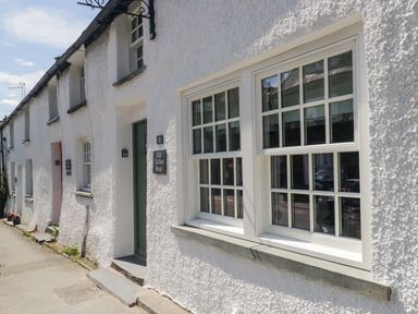 A row of white rendered cottages with windows and doors on a sidewalk at Old Toffee Shop in Ambleside