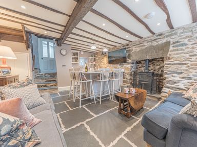 A living room with stone walls wooden beams a wood stove and a kitchen island with chairs at Old Toffee Shop Ambleside