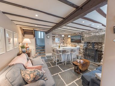 A living area with sofas pillows a small wooden table kitchen island stools and a stove at Old Toffee Shop in Ambleside
