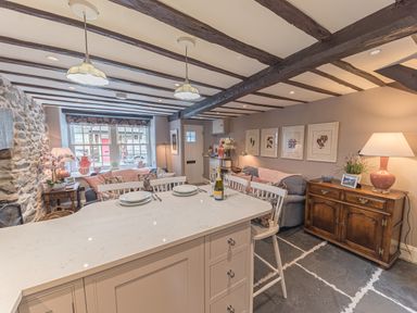 A kitchen island with plates and a bottle next to chairs in a room with exposed beams and stone walls at Old Toffee Shop in Ambleside