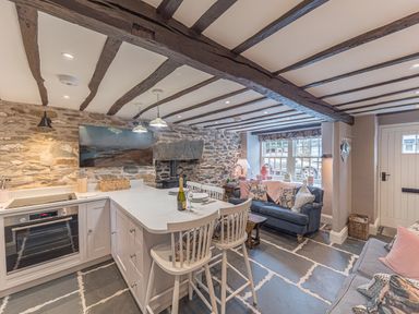 A kitchen and living area with stone walls wooden beams bar stools and sofas at Old Toffee Shop Ambleside