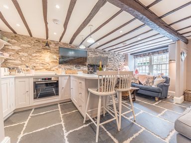 A kitchen with stone walls wooden beams a grey sofa and two white chairs at Old Toffee Shop in Ambleside