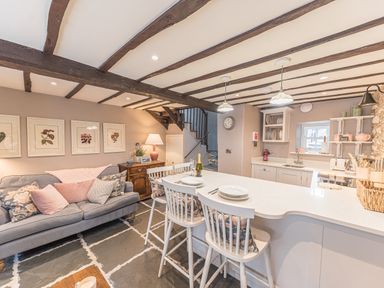 An open plan kitchen and living area with a gray sofa and white bar stools at Old Toffee Shop in Ambleside