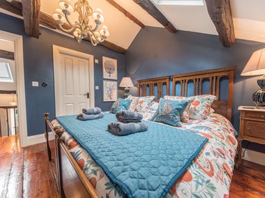 A bedroom with a wooden bed a blue quilt folded towels on the bed and a chandelier at Old Toffee Shop Ambleside