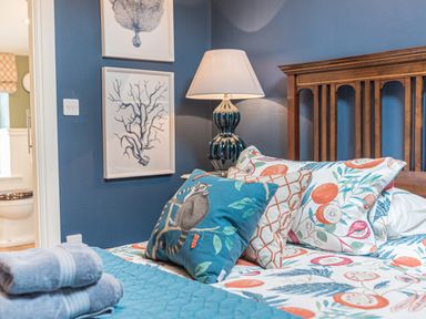 A bedroom with a wooden headboard, patterned pillows, a lamp on a bedside table, and framed art on a blue wall at Old Toffee Shop in Ambleside