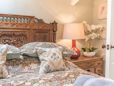 A bedroom with a carved wooden headboard patterned bedding a bedside table lamp and flowers at Old Toffee Shop in Ambleside