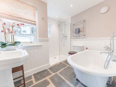 A bathroom with a freestanding bathtub a glass shower a toilet a sink and a window with a beige blind at Old Toffee Shop in Ambleside