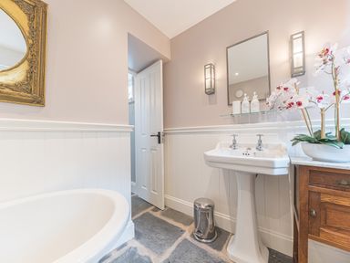 A bathroom with a white bathtub a pedestal sink a wooden cabinet with flowers and a mirror at Old Toffee Shop in Ambleside