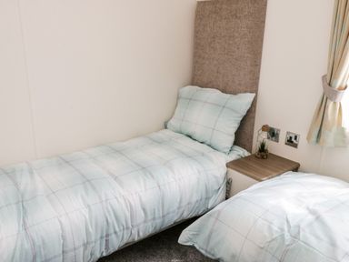 A bedroom with two beds a small nightstand with a decorative item and a window with curtains at The Rodley Pines in Cayton