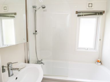 A bathroom with a sink and faucet a bathtub with showerhead and glass screen a window with blinds and a rubber duck at The Rodley Pines in Cayton