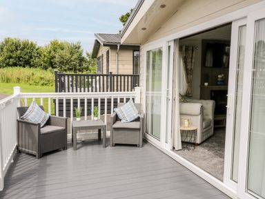 An outdoor patio with two chairs a small table and potted plants next to a sliding glass door leading to a living room at The Rodley Pines in Cayton
