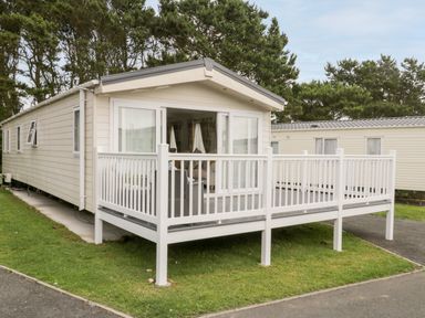 A beige mobile home with a white railing porch and sliding glass doors surrounded by trees at The Rodley Pines in Cayton