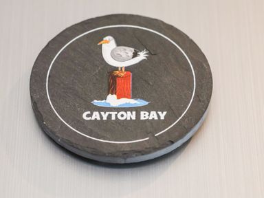 A circular coaster with a seagull standing on a red post and the words Cayton Bay
