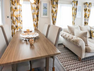 A dining table with chairs next to a sofa with cushions in a room with patterned curtains at The Rodley Pines in Cayton