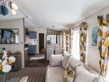 An open plan living room and kitchen with a beige sofa dining table with chairs and yellow patterned curtains at The Rodley Pines in Cayton